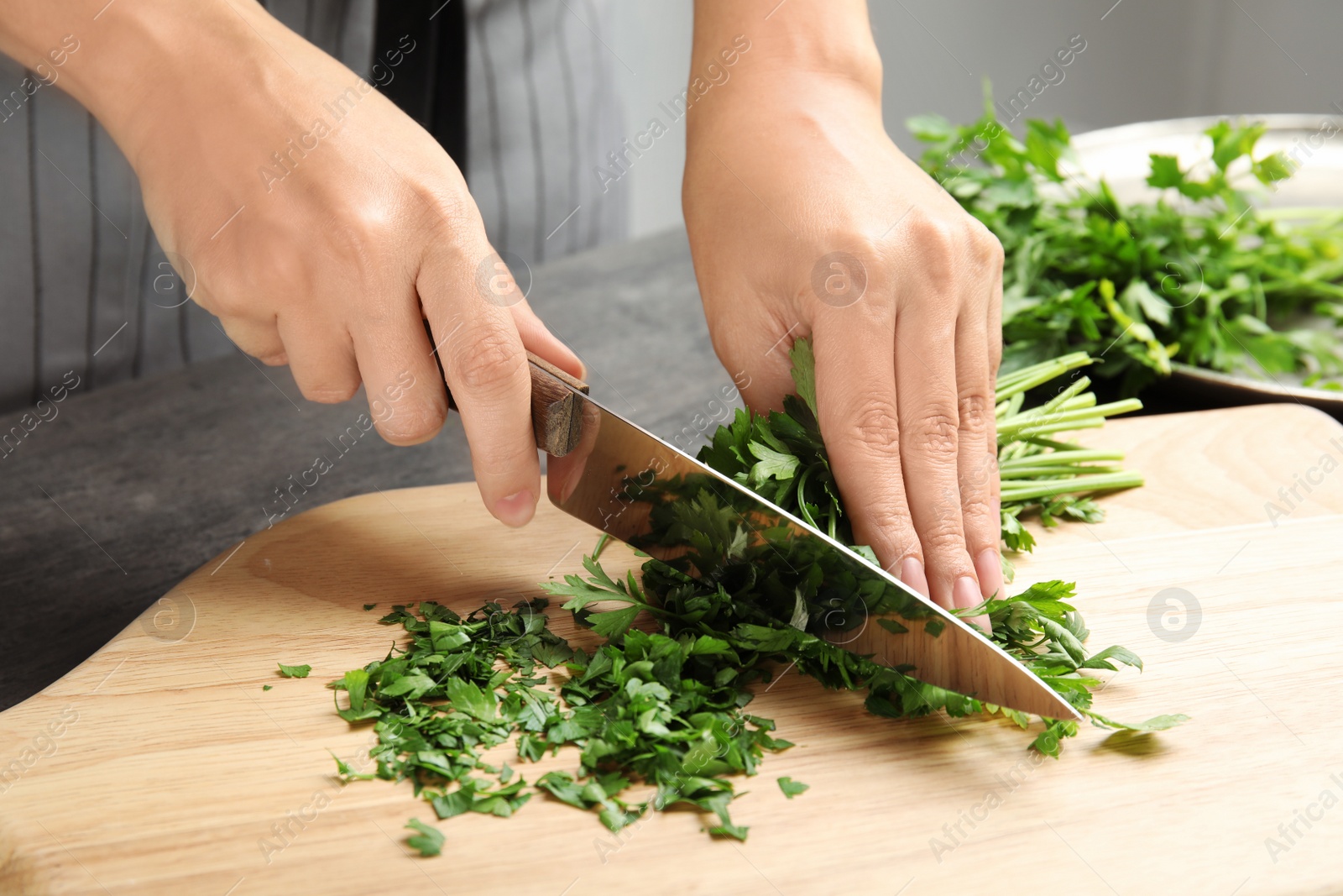 Photo of Woman cutting fresh green parsley on wooden board, closeup