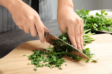 Photo of Woman cutting fresh green parsley on wooden board, closeup