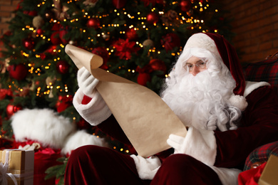 Santa Claus reading wish list in armchair near Christmas tree