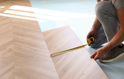 Photo of Worker installing laminated wooden floor indoors, closeup