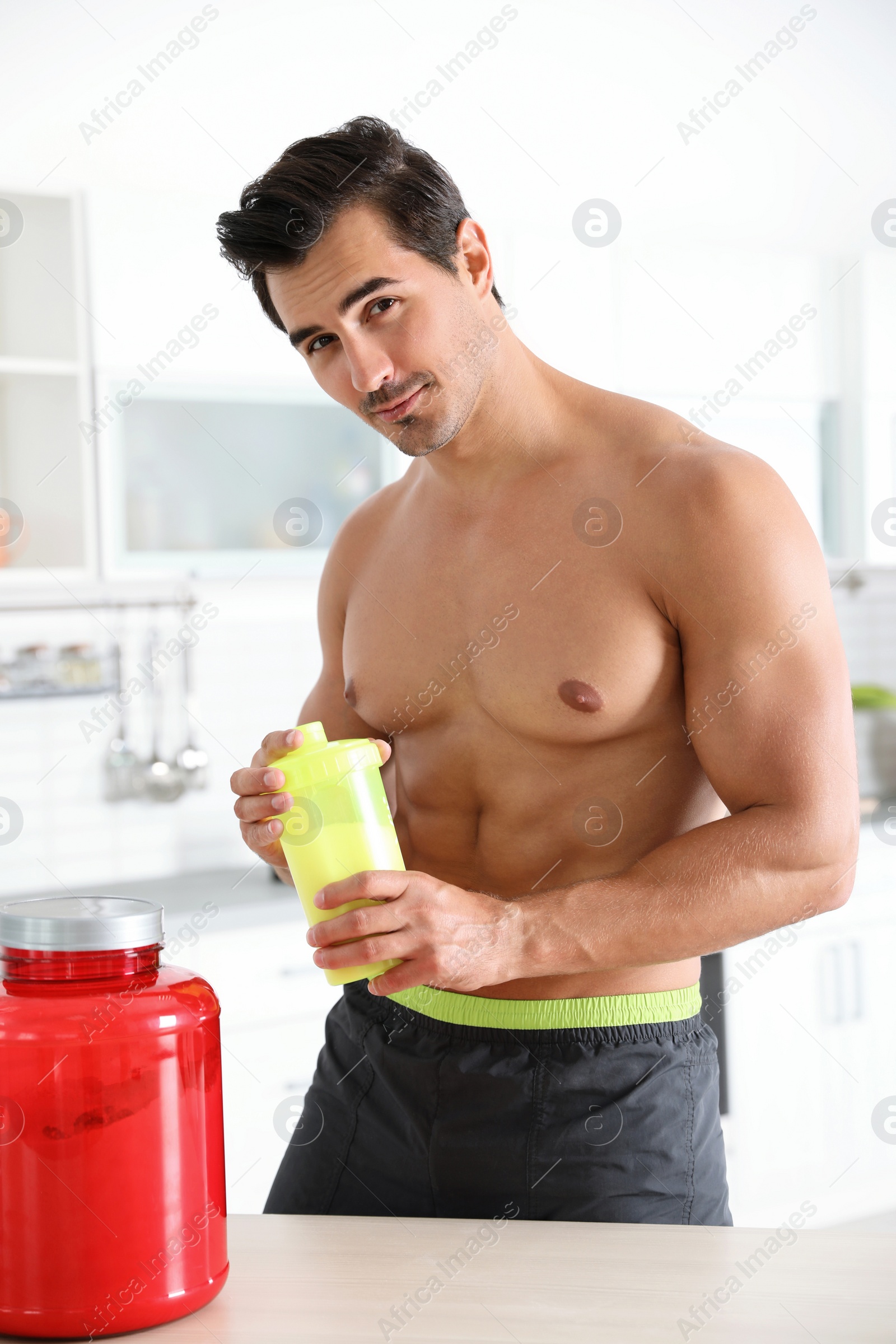 Photo of Young shirtless athletic man with protein shake powder in kitchen