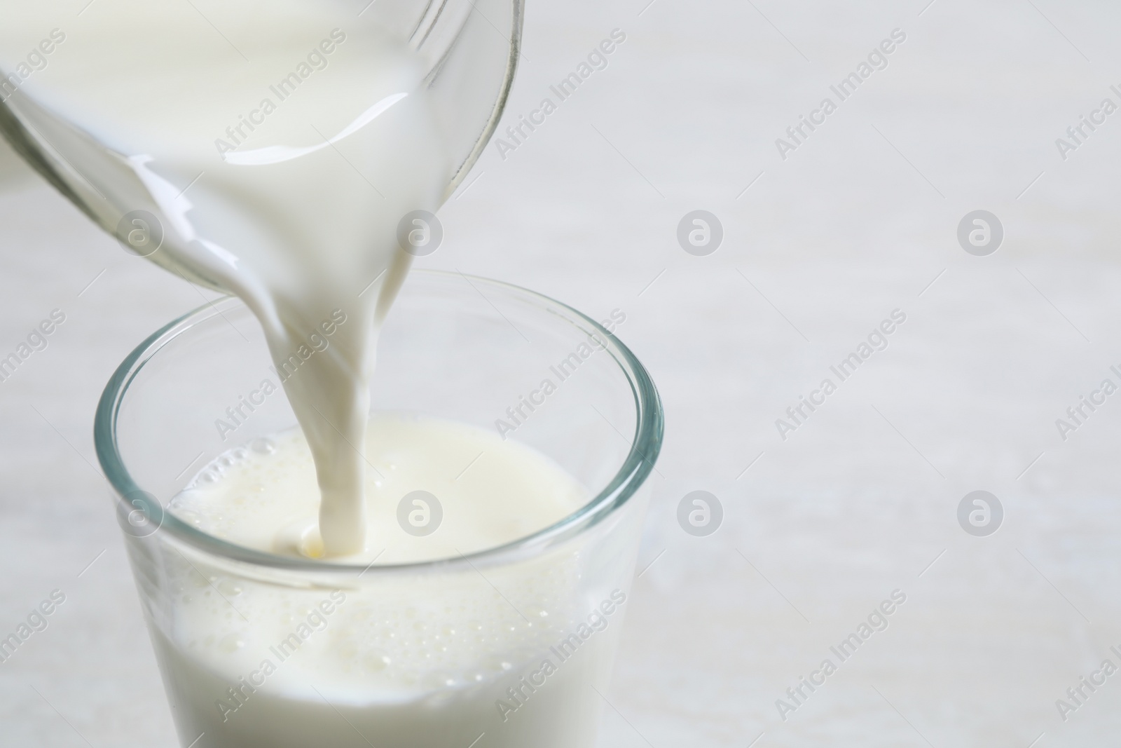 Photo of Pouring milk into glass on white table, closeup. Space for text