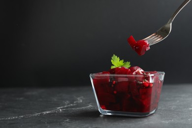 Photo of Pickled beets and fork over glass bowl on dark marble table, space for text