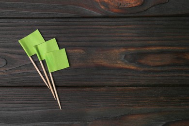 Photo of Small green paper flags on wooden table, flat lay. Space for text