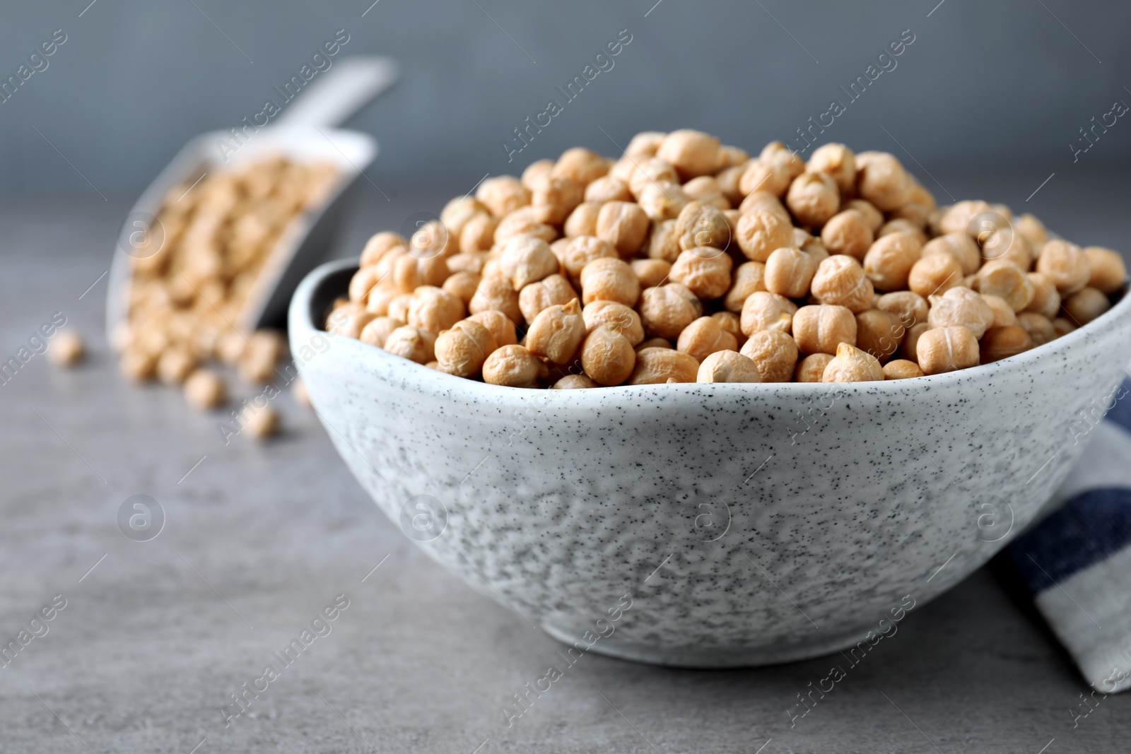 Photo of Raw chickpeas in bowl on grey table, closeup