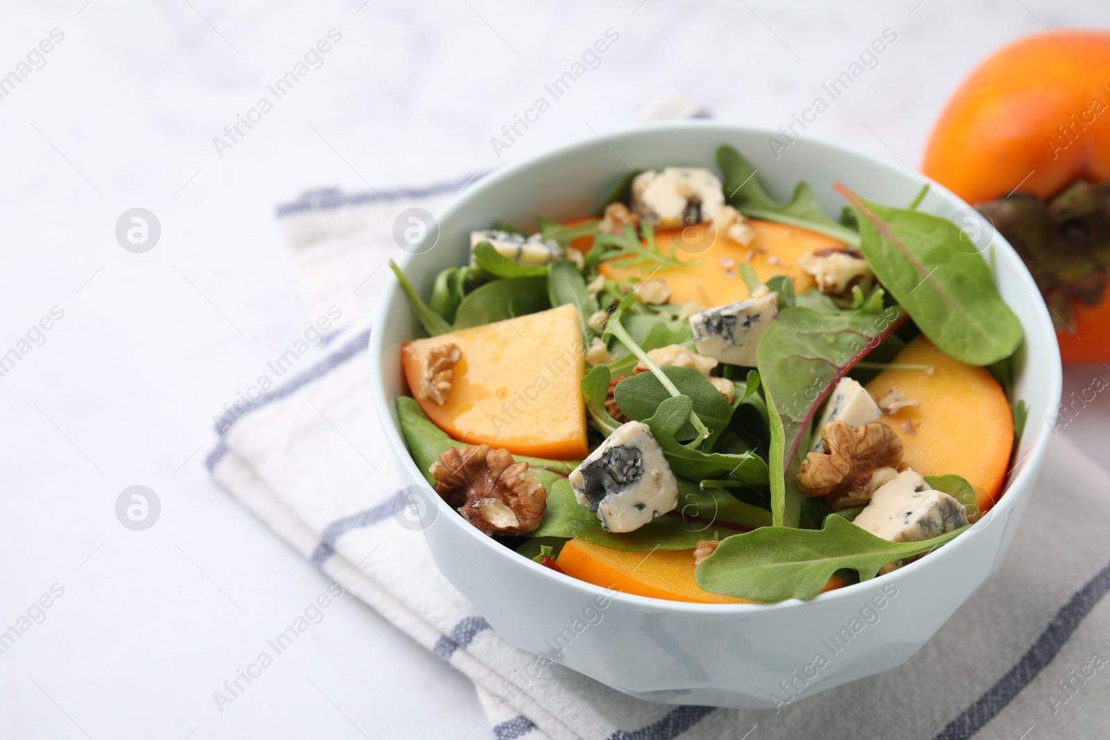 Photo of Tasty salad with persimmon, blue cheese and walnuts served on white table, closeup. Space for text