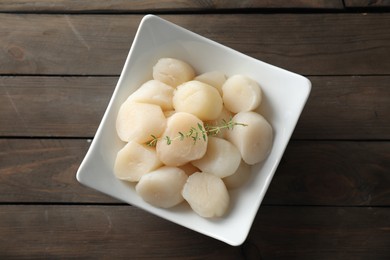 Photo of Fresh raw scallops and thyme in bowl on wooden table, top view