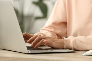 African-American woman typing on laptop at wooden table indoors, closeup