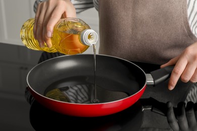 Photo of Woman pouring cooking oil from bottle into frying pan on stove, closeup