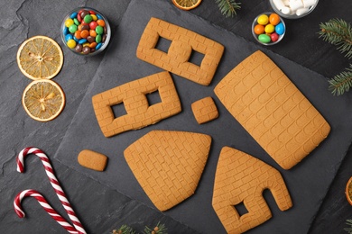 Photo of Parts of gingerbread house, fir tree branches and ingredients on black table, flat lay