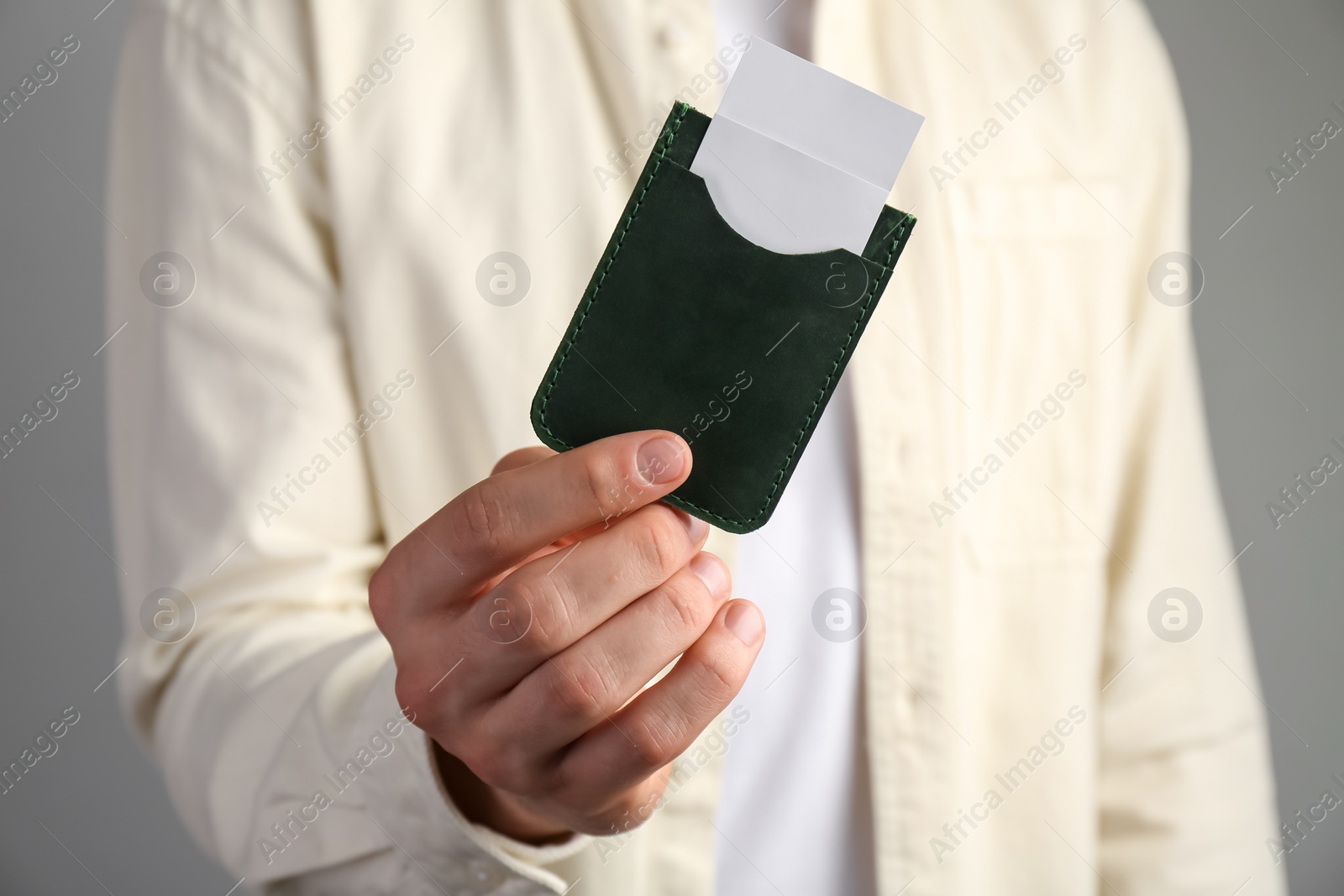 Photo of Man holding leather business card holder with cards on grey background, closeup