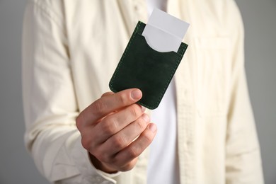 Man holding leather business card holder with cards on grey background, closeup