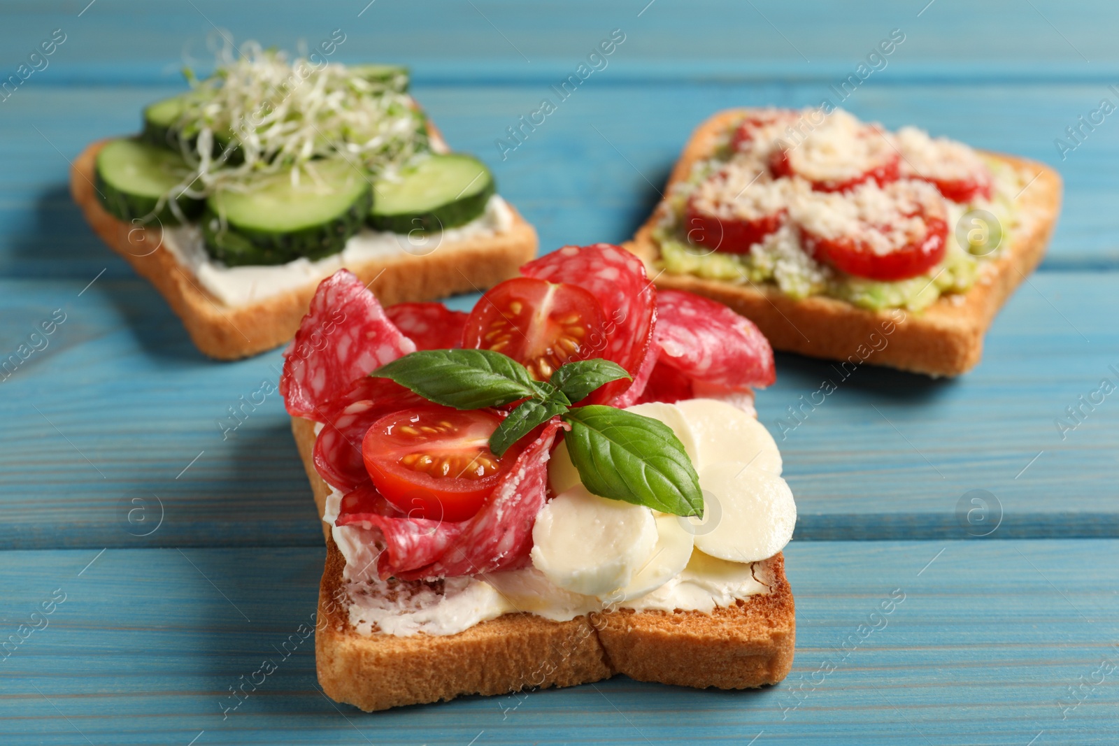 Photo of Tasty toasts with different toppings on light blue wooden table, closeup