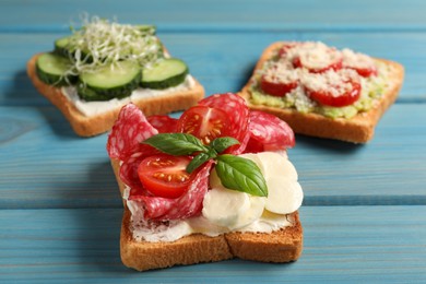 Tasty toasts with different toppings on light blue wooden table, closeup