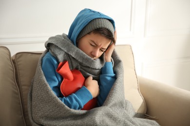 Photo of Sick teenage boy wrapped in blanket with hot water bottle on sofa at home