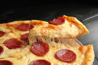 Photo of Taking slice of tasty pepperoni pizza on black table, closeup