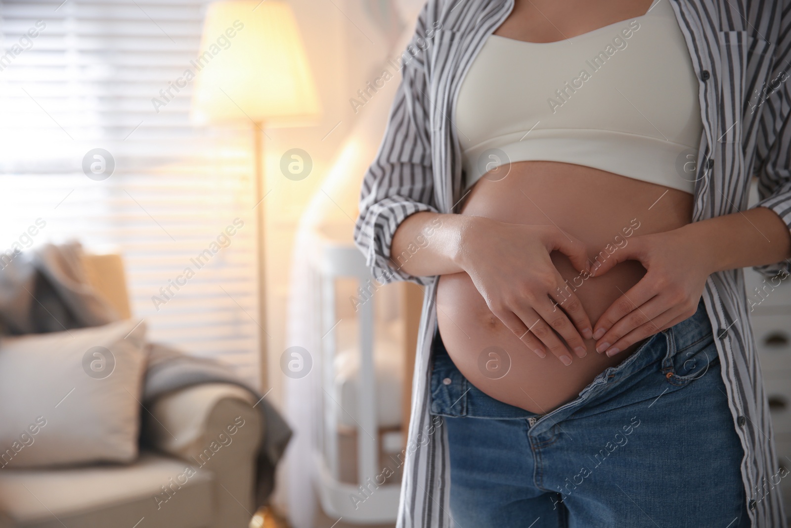 Photo of Pregnant woman making heart with her hands near belly indoors, closeup