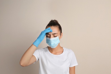 Stressed woman in protective mask on beige background. Mental health problems during COVID-19 pandemic