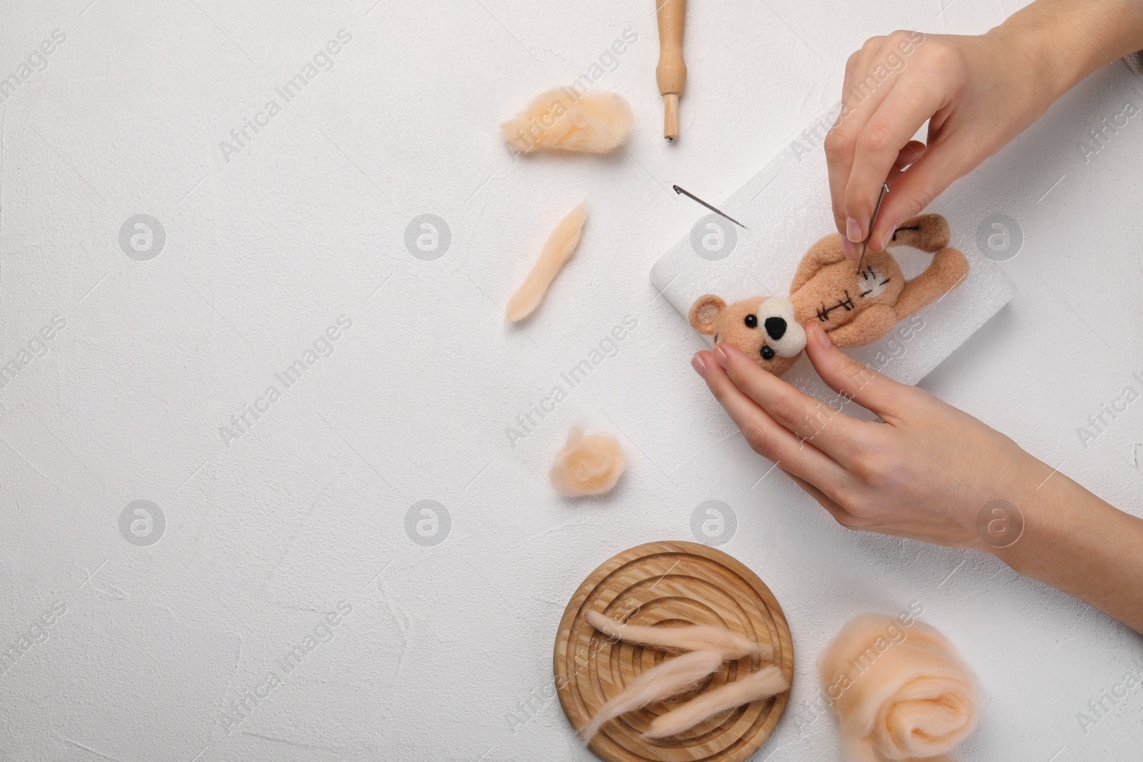 Photo of Woman felting toy bear from wool at white table, top view. Space for text