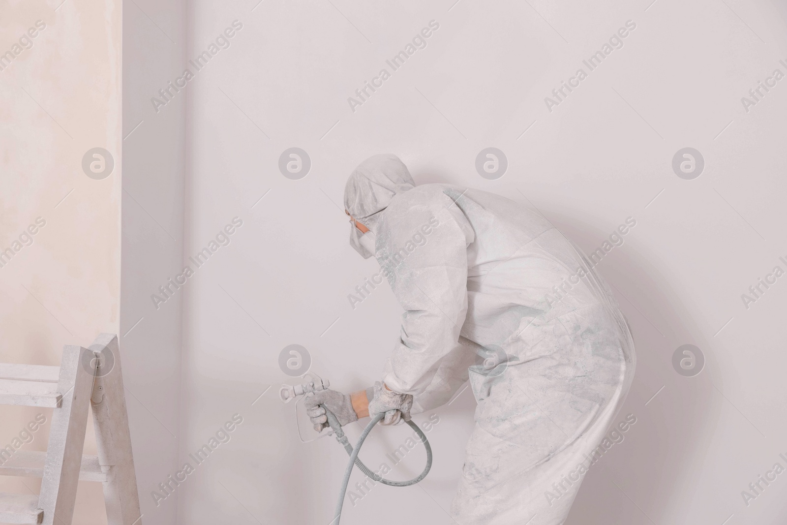 Photo of Decorator in uniform painting wall with sprayer indoors