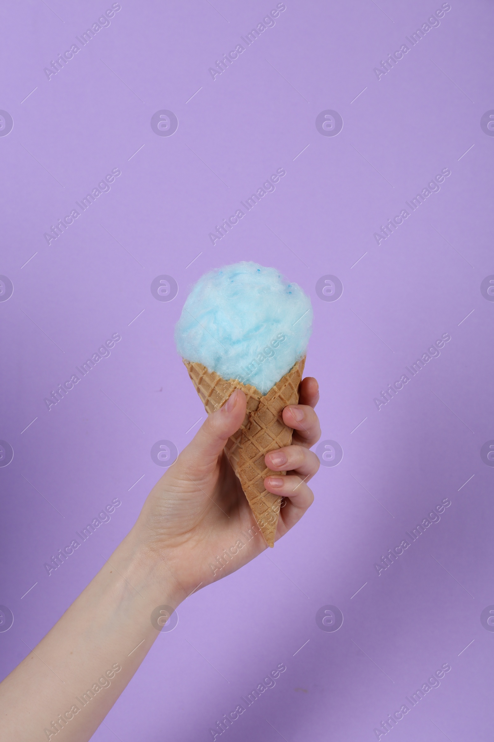 Photo of Woman holding waffle cone with cotton candy on violet background, closeup