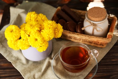 Beautiful yellow chrysanthemum flowers, cup of aromatic tea and sweet chocolate treats on wooden table