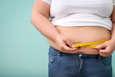 Photo of Overweight woman with measuring tape on color background