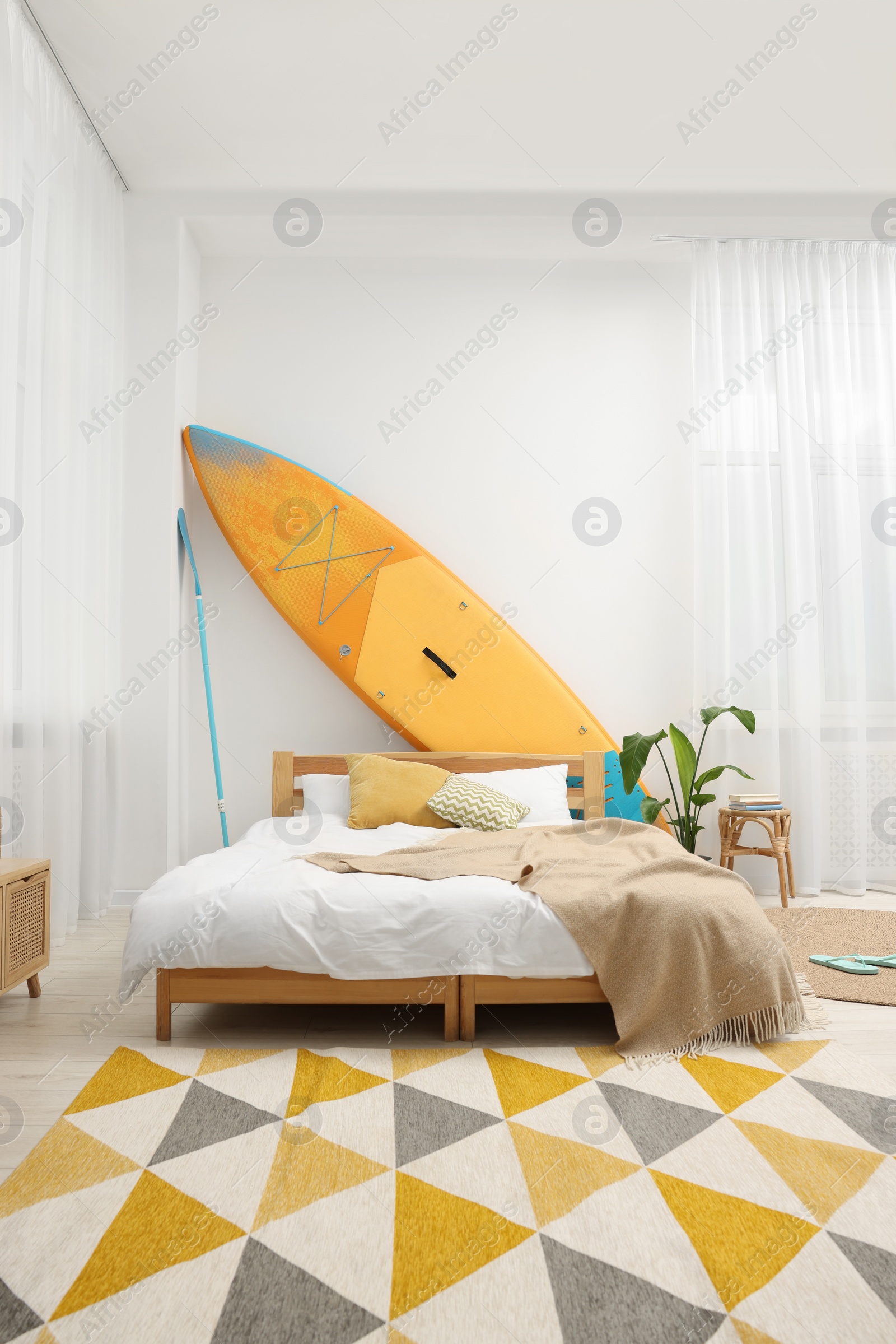 Photo of Large comfortable bed, SUP board and green houseplant in stylish bedroom. Interior design