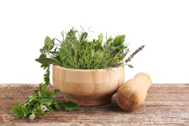 Photo of Mortar, pestle and different herbs on wooden table against white background