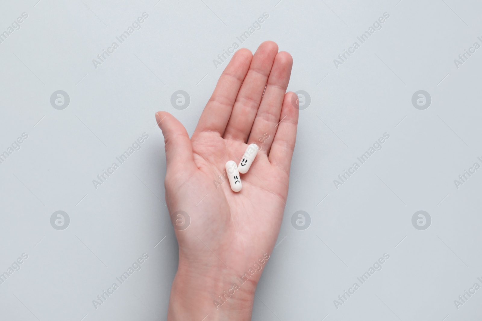 Photo of Woman holding antidepressants with emoticons on grey background, top view