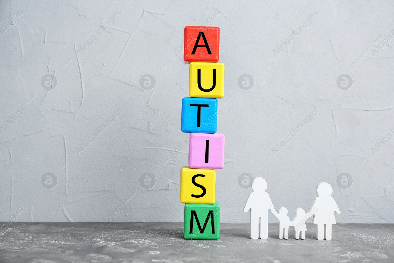 Photo of Colorful cubes with word AUTISM and figure of family on table against grey background