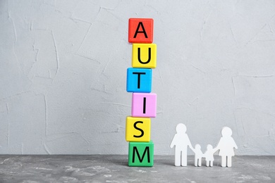 Photo of Colorful cubes with word AUTISM and figure of family on table against grey background