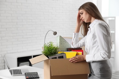 Photo of Upset young woman packing stuff in box at office