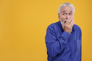 Photo of Embarrassed senior man covering mouth with hand on orange background. Space for text
