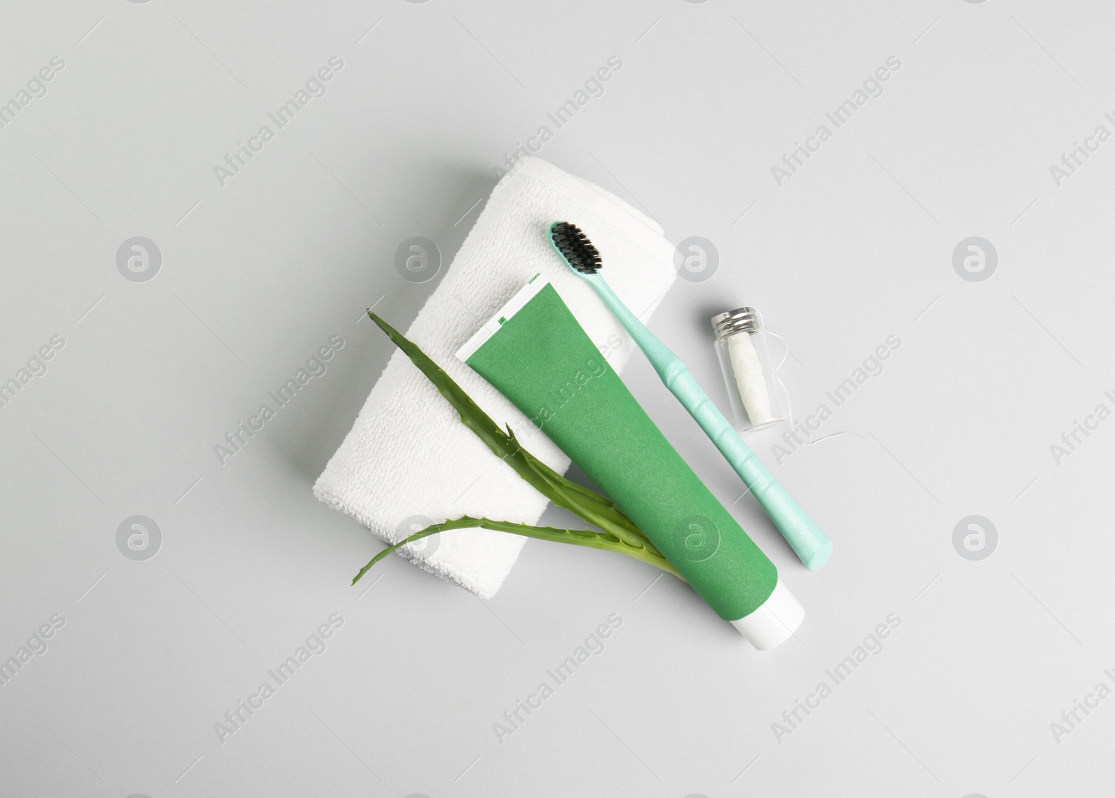 Photo of Tube of toothpaste, toothbrush, dental floss, towel and fresh aloe on light grey background, flat lay