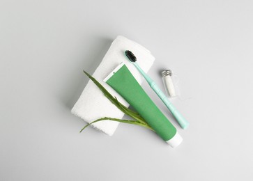 Tube of toothpaste, toothbrush, dental floss, towel and fresh aloe on light grey background, flat lay