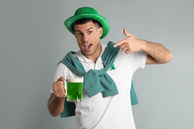 Photo of Emotional man in St Patrick's Day outfit with beer on light grey background