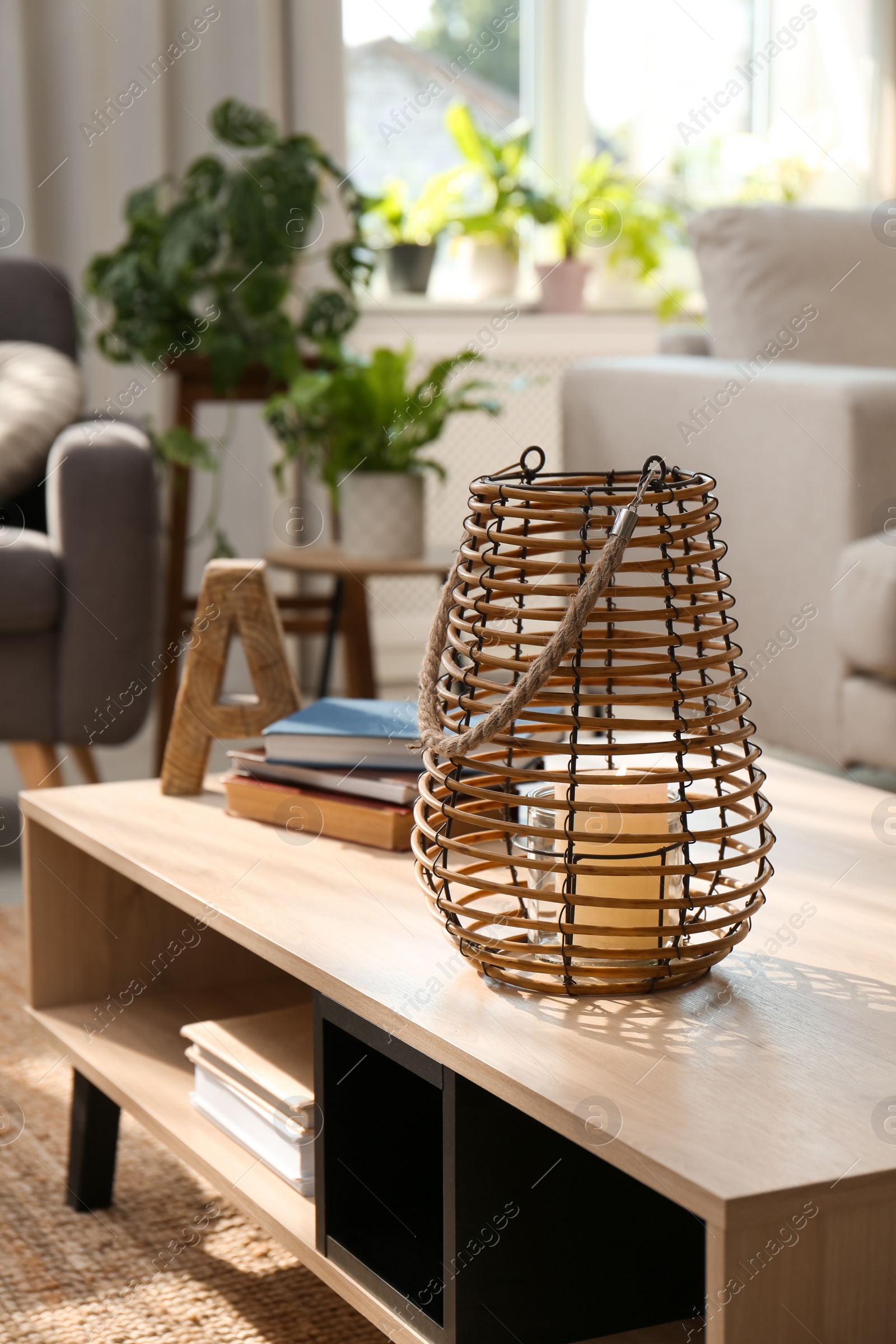 Photo of Stylish holder with burning candle and books on wooden table in living room