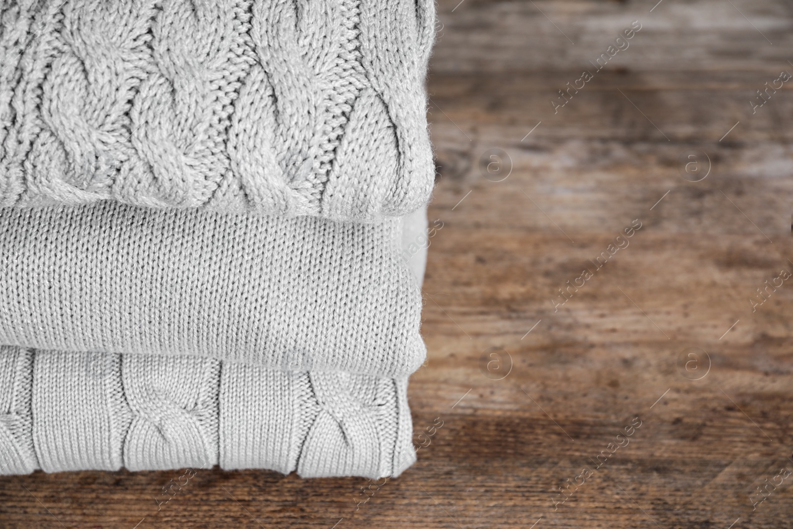 Image of Stack of folded warm sweaters on wooden table. Space for text