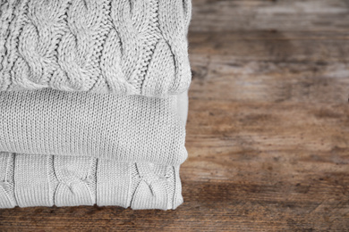 Stack of folded warm sweaters on wooden table. Space for text