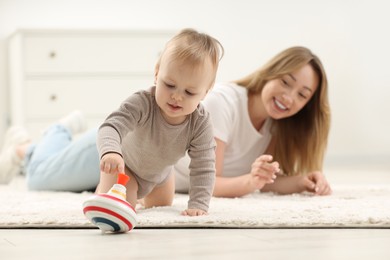Photo of Children toys. Happy mother and her little son playing with spinning top on rug at home, selective focus