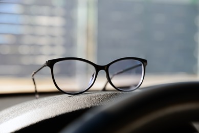 Photo of New stylish glasses on dashboard in car
