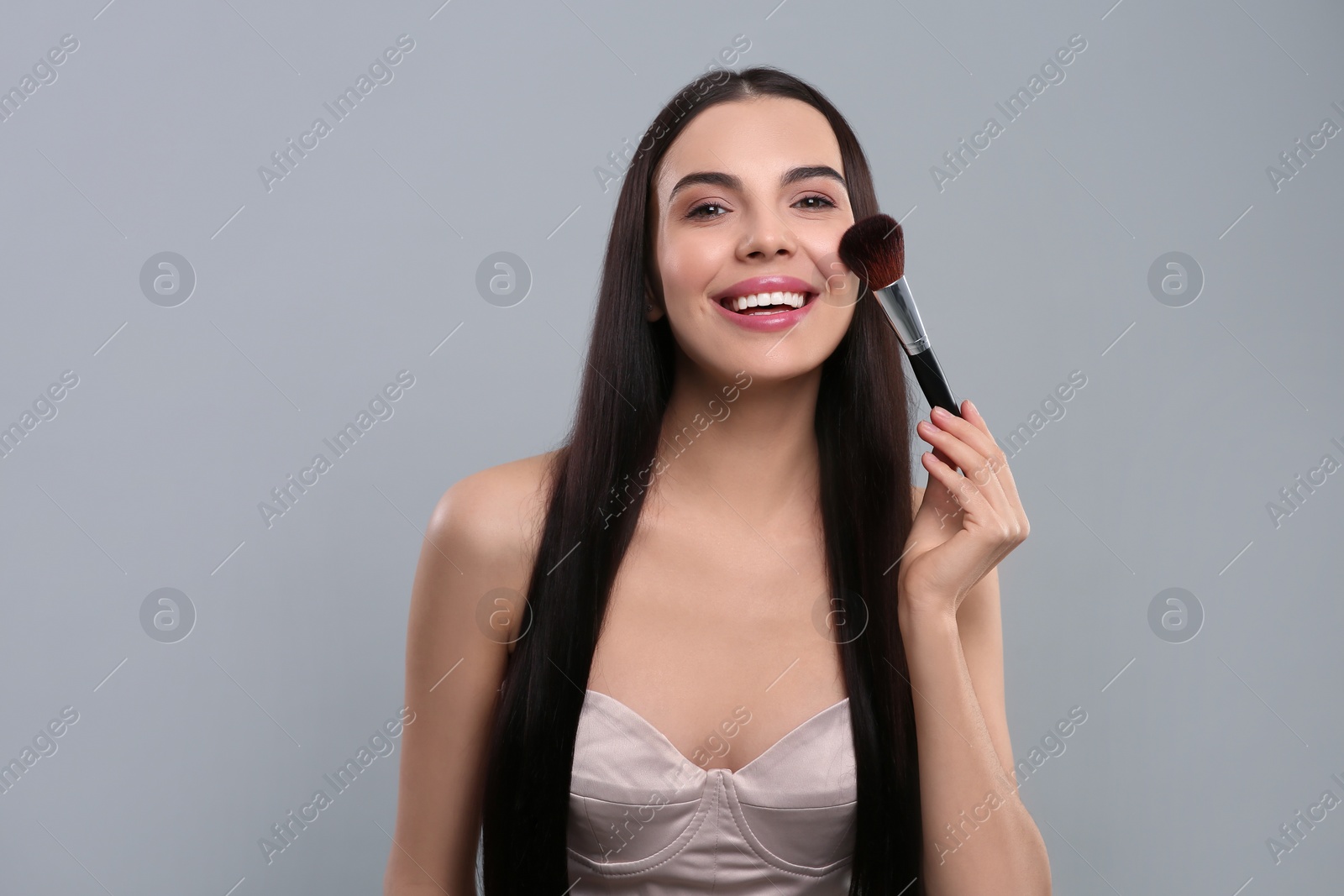 Photo of Happy woman applying makeup on light grey background