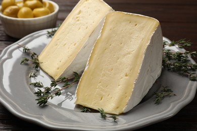 Photo of Pieces of tasty camembert cheese and thyme on table, closeup