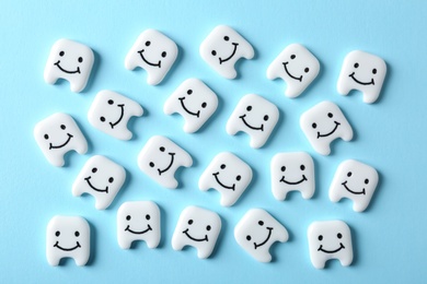Many small plastic teeth with cute faces on color background, top view