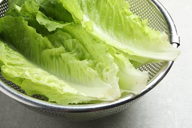 Photo of Colander with fresh leaves of green romaine lettuce on light grey table, closeup