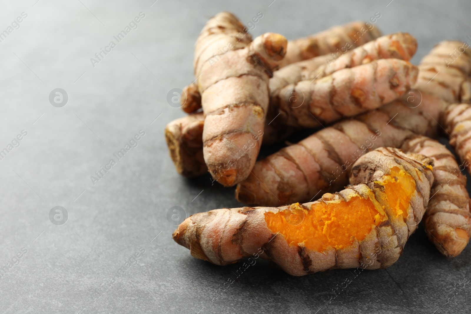 Photo of Many raw turmeric roots on grey table, closeup. Space for text
