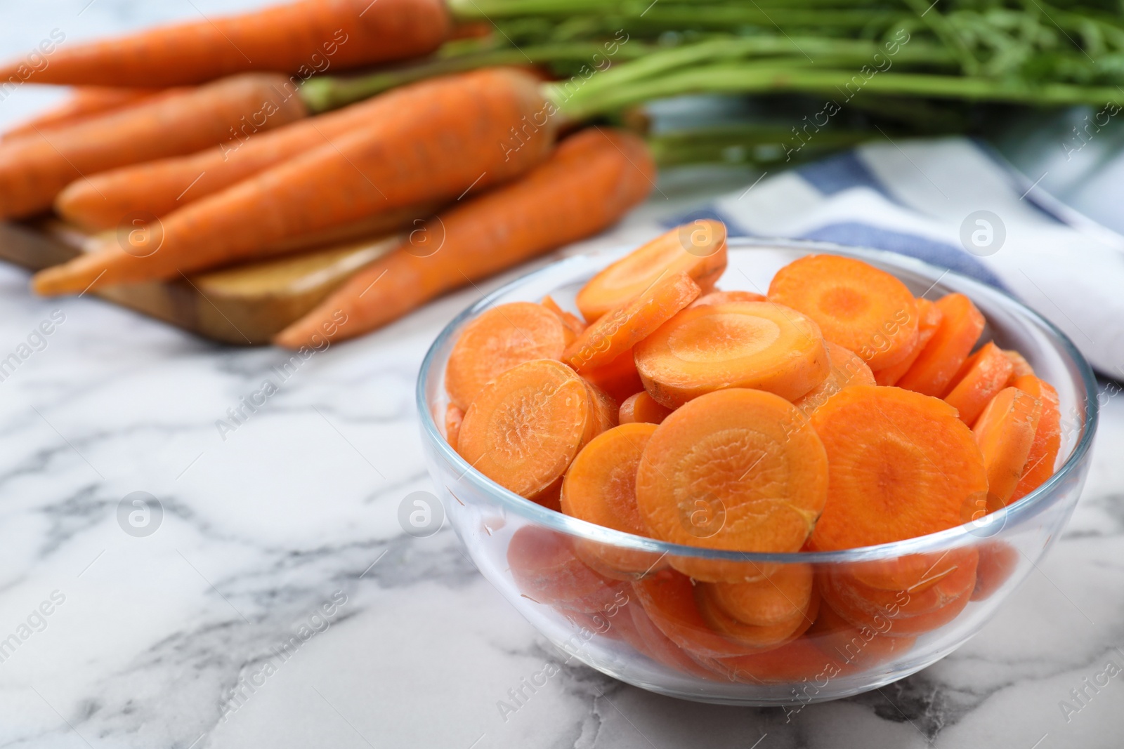 Photo of Slices of ripe carrots in glass bowl on white marble table, closeup