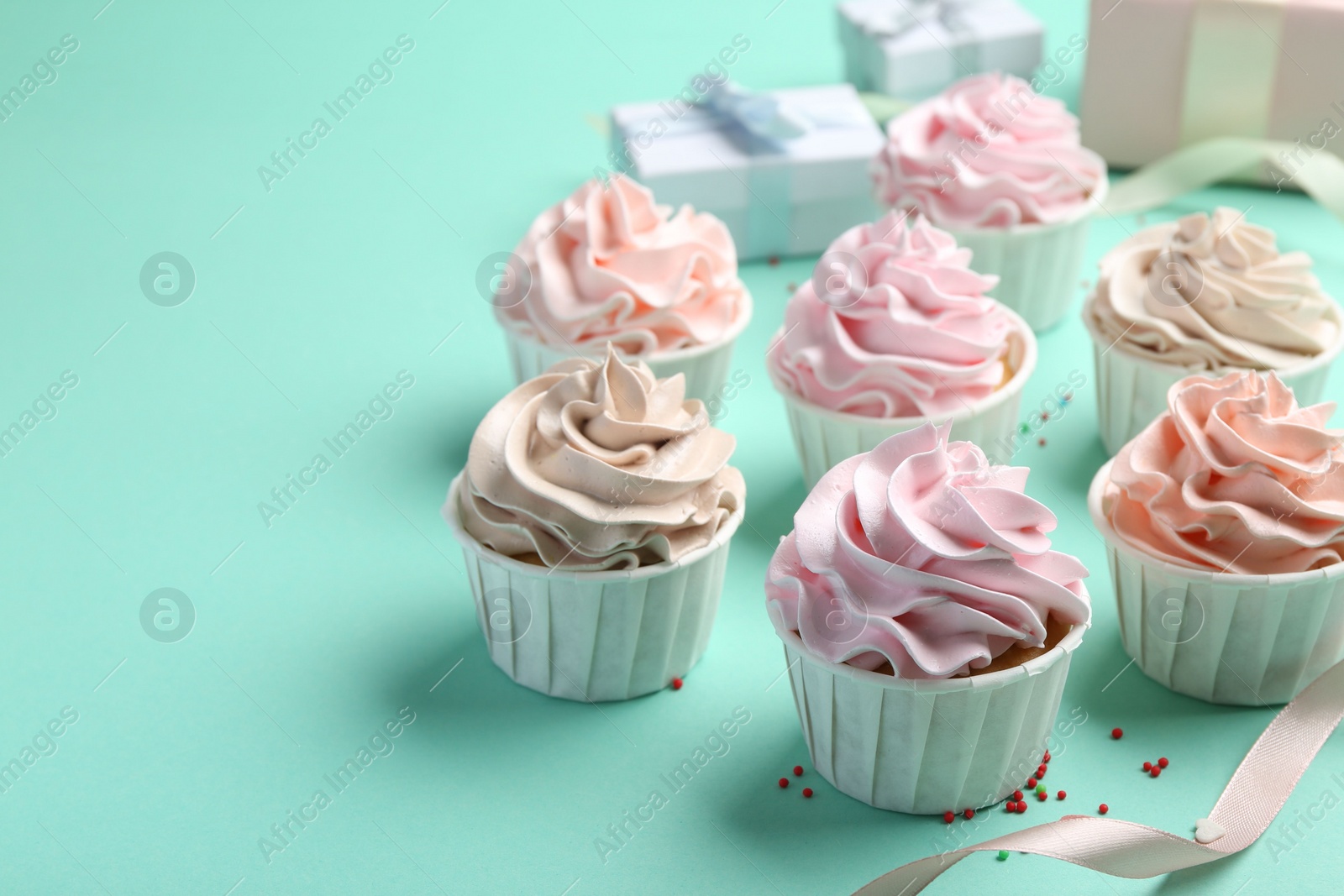 Photo of Delicious birthday cupcakes, ribbon and sprinkles on turquoise background, closeup. Space for text