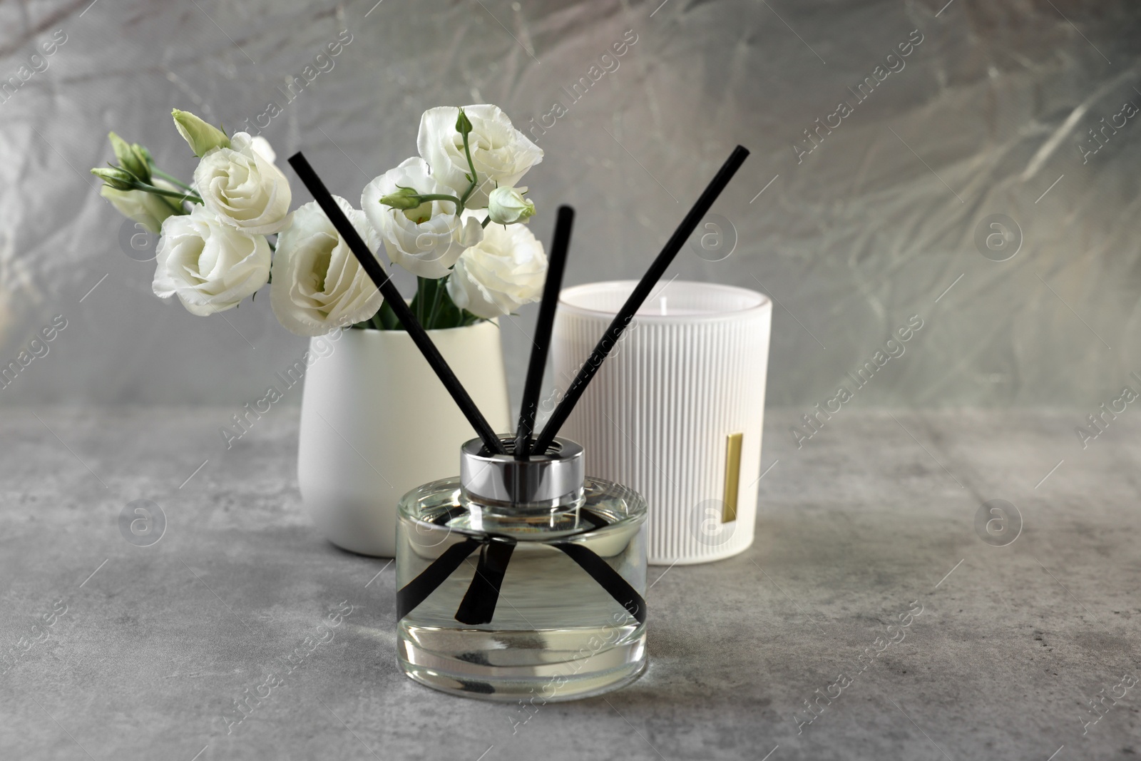 Photo of Reed diffuser, scented candle and eustoma flowers on gray marble table